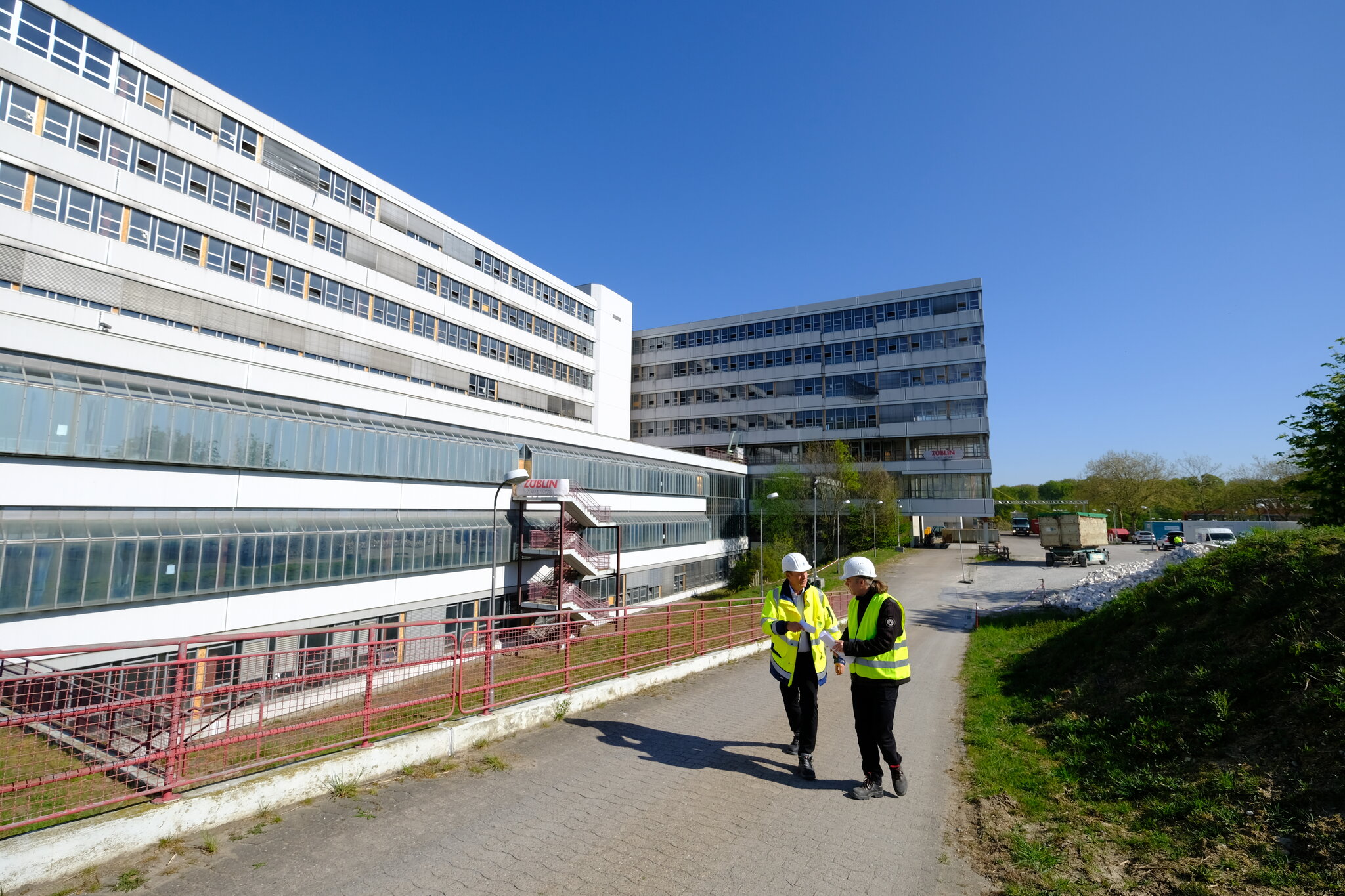 Zwei BLB-Mitarbeiter laufen am Gebäude entlang